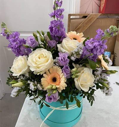 Breakfast at Tiffany's - A modern arrangement presented in a hatbox in a mix of purple, white and green flowers. This is due to impress your recipient. Created and delivered my Moody Cows Florist in Carluke. Please note: colour of the hatbox may vary.